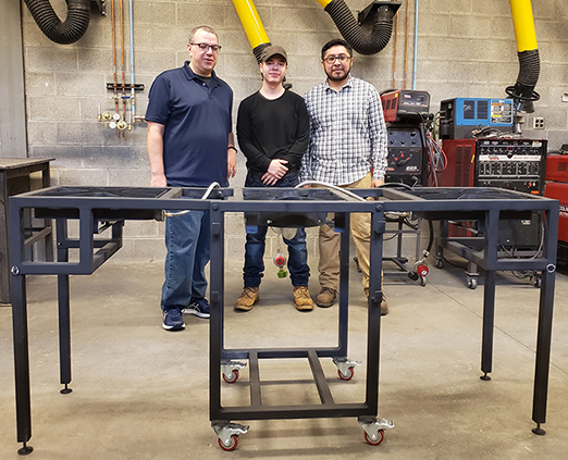 three males standing in front of a metal stand